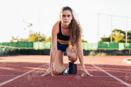 Preview: A female athlete getting ready to run on an athletics track.