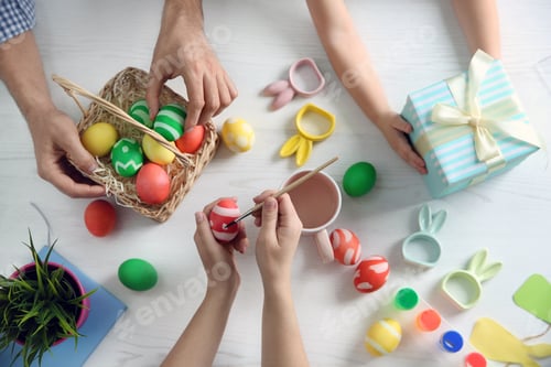 Preview: Father, mother and their child painting Easter eggs on wooden background, top view