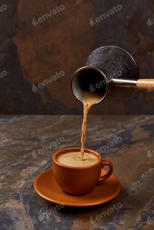 Preview: pouring coffee from cezve into brown cup on marble surface
