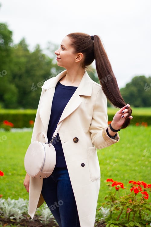 Preview: A young girl stands in the spring in a light coat, looks to the side, holds her long hair