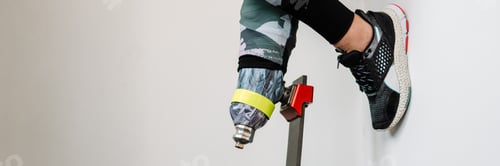 Preview: Young sportswoman with prosthesis leaning on wall indoors