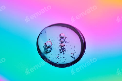 Preview: A drop of cosmetic serum on a multicolored background in shades of blue and lilac.