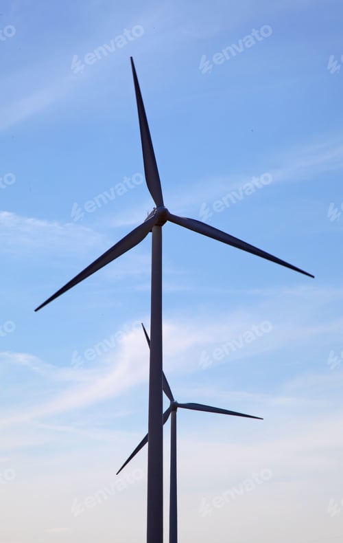 Preview: Vertical closeup shot of wind turbines against a light blue sky