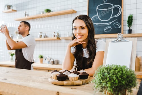 Preview: attractive brunette waitress standing behind bar with cupcakes on wooden tray wile barista holding