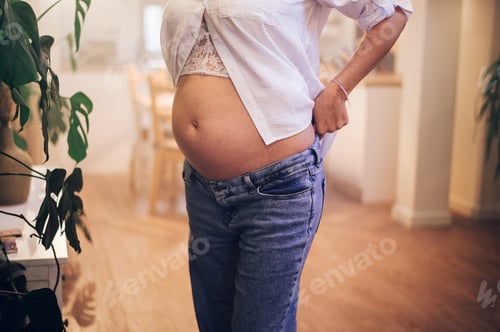 Preview: Cropped shot of pregnant woman standing at home holding hands on her belly