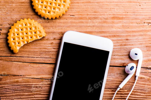 Preview: Smartphone, earphones and biscuits laid on old office desk