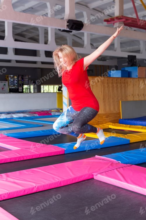 Preview: Fitness, fun, leisure and sport activity concept - Young happy woman jumping on a trampoline indoors