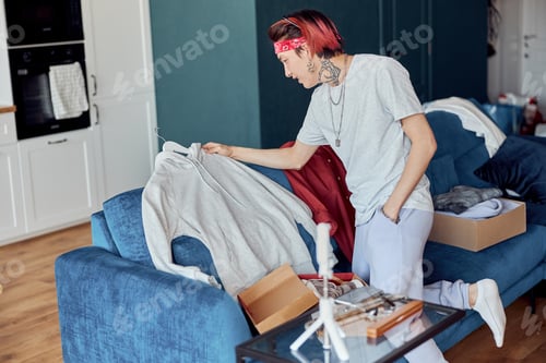 Preview: Smiling Asian guy unpacking online shopping at home, holding hoodie
