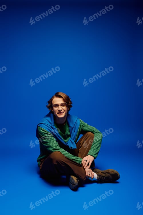 Preview: Charming young man seamlessly blends style and personality in a vibrant blue backdrop