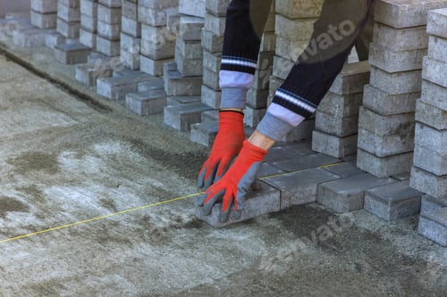 Preview: The master in gloves lays paving stones in layers pathway paving by professional paver worker.