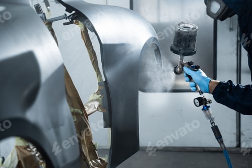 Preview: Auto mechanic spraying dark paint on vehicle body with professional coating tools