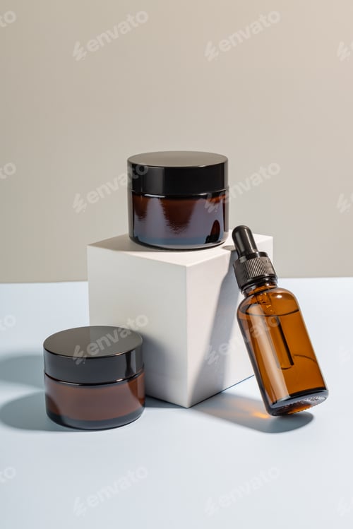 Preview: Beauty face serum in a glass dropper bottle and cream jars on white cube podium. Hyaluronic acid oil