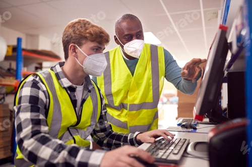 Preview: Male Intern With Supervisor Wearing Face Masks Working In Busy Modern Warehouse On Computer Terminal