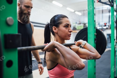 Preview: Young woman power lifting helped by her personal trainer
