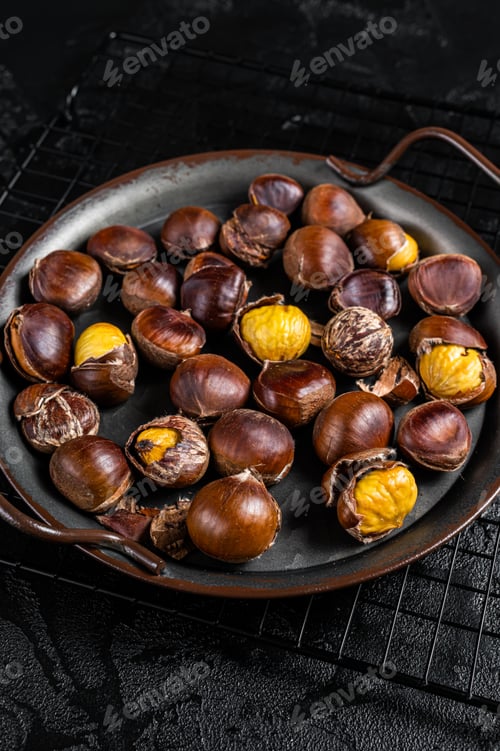 Preview: Cracked roast chestnuts served in a tray. Black background. Top view