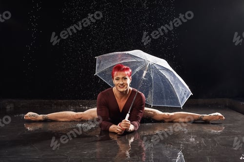 Preview: Beautiful young girl in red sportswear with umbrella in aqua studio. Drops of water spread about her