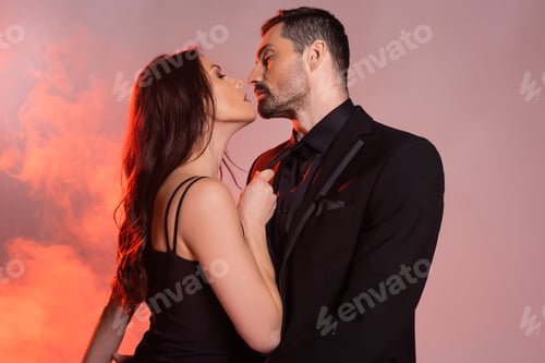 Preview: sexy woman in black dress pulling tie while seducing man in formal wear on pink and grey