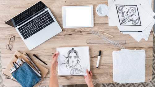 Preview: overhead view of female designer putting white t-shirt with print on table with digital devices an