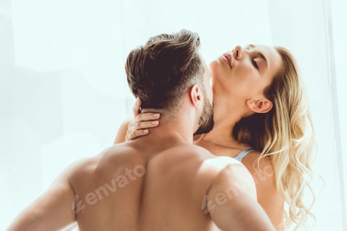Preview: back view of shirtless man kissing sensual girlfriend near window at home