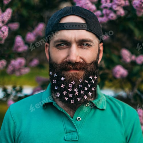 Preview: A bearded man with a lilac flowers decorated beard for the Spring holiday