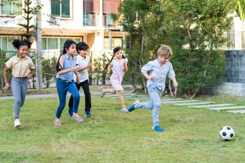 Preview: Group of young children playing football outdoors in the school garden.
