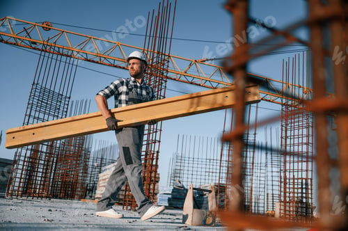 Preview: Walking and holding wooden plank. Man is working on the construction site at daytime