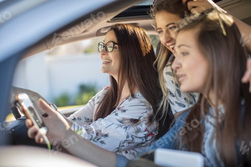 Preview: Three women smiling in a car with one holding a smartphone