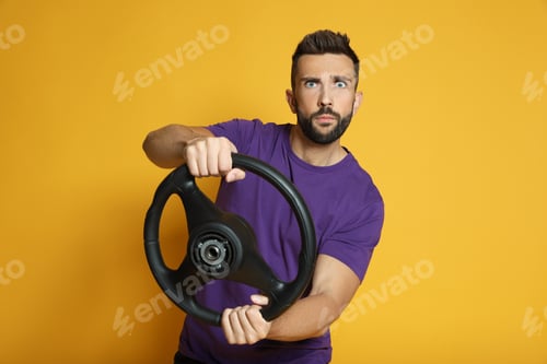 Preview: Serious man with steering wheel on yellow background