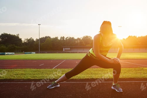 Preview: Young female runner stretching on sunlit race track