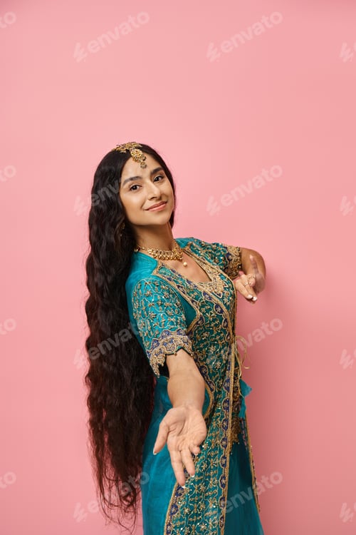 Preview: attractive young female model in blue traditional sari looking at camera posing on pink backdrop
