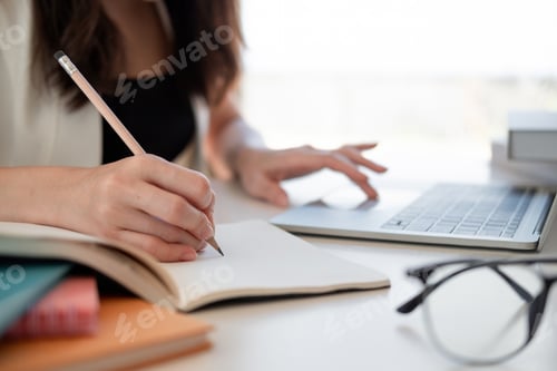 Preview: Close up woman's hands with laptop computer, notebook and pen taking notes in business office