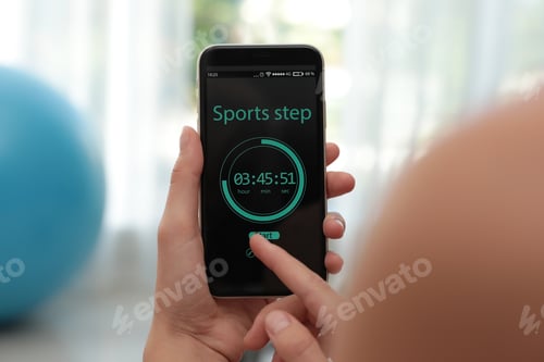 Preview: Young woman using fitness app on smartphone indoors, closeup