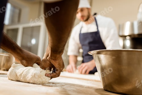 Preview: cropped shot of bakers kneading dough together at baking manufacture