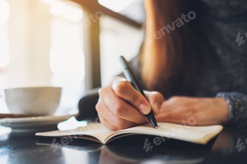 Preview: Closeup image of a woman writing on a blank notebook on the table