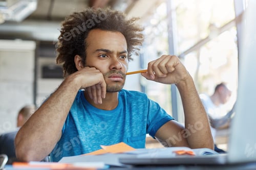 Preview: Pensive male freelancer sitting at coffee shop looking with serious expression in laptop working wit