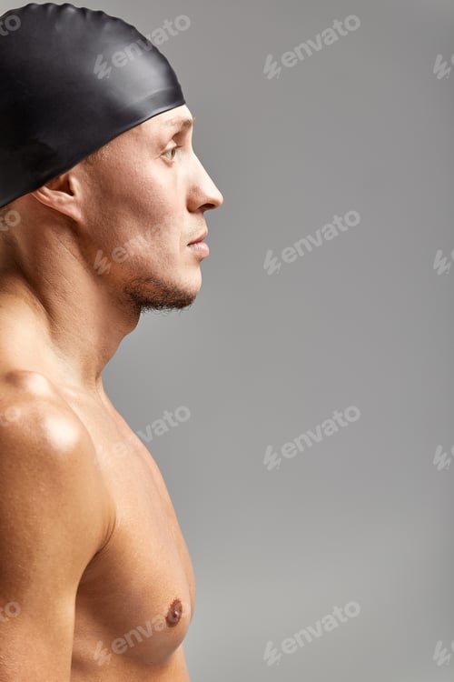 Preview: portrait of a young man swimmer wearing a rubber hat, standing against a gray background hat getting