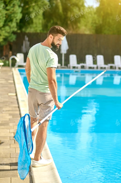 Preview: A dark-haired man cleaning the swimming pool and looking busy