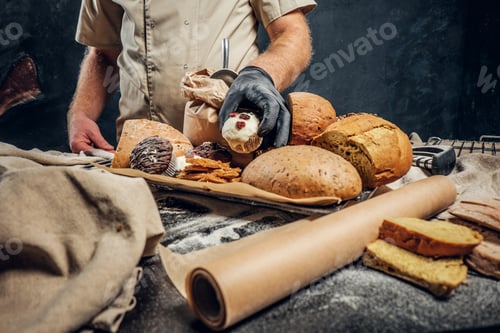 Preview: Bearded baker wearing a uniform standing next to a table with delicious bread loaves, baguettes