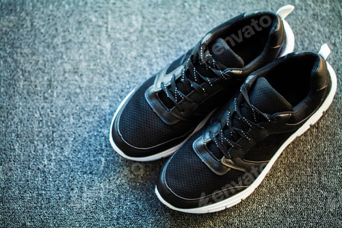 Preview: Pair of new stylish black sneakers on floor at home