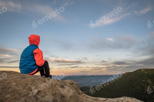 Preview: Young child boy hiker sitting in mountains enjoying view of amazing mountain landscape.