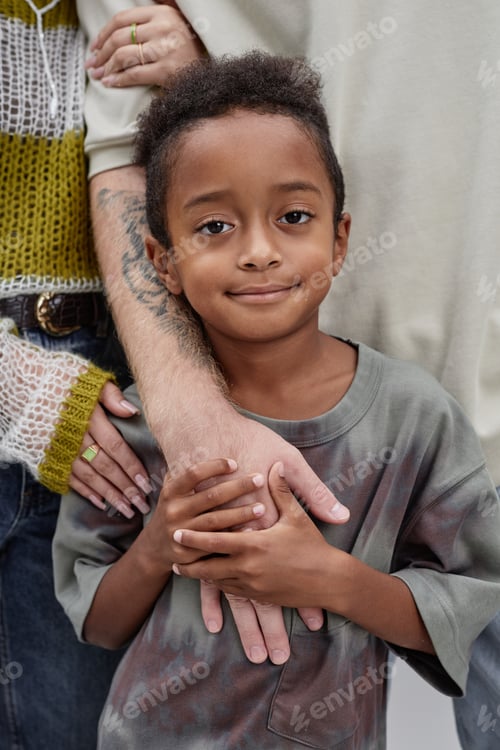 Preview: Portrait of Smiling Adopted Black Boy Holding Parents Hands in Studio