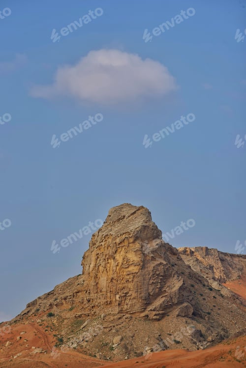 Preview: Idyllic view of a red sand mountainous rock formation beneath a blue sky and solitary puffy cloud