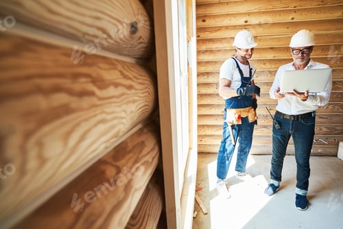 Preview: Architect and worker in wooden house checking data on laptop