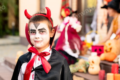 Preview: Cute boy with painted face in costume of devil sitting in front of camera