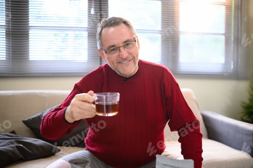 Preview: Happy retired man relaxing indoors with a glass cup of coffee in hand