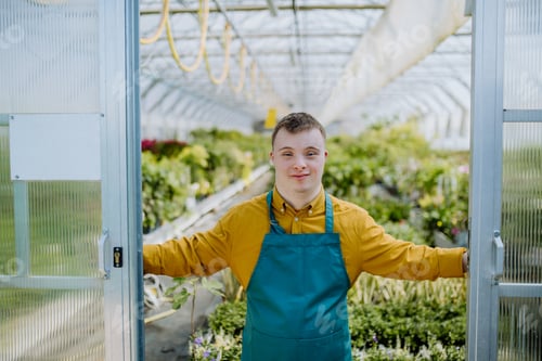 Preview: Young employee with Down syndrome working in garden centre, looking at camera and standing in door