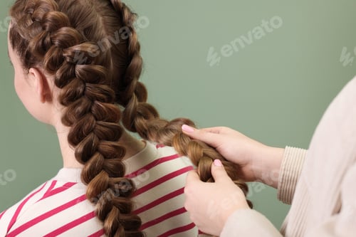 Preview: Professional stylist braiding woman's hair on olive background, closeup