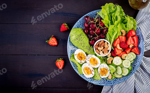 Preview: Plate with a paleo diet food. Boiled eggs, avocado, cucumber, nuts, cherry and strawberries