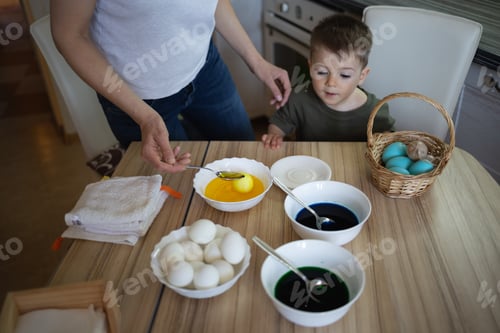 Preview: little cute boy paints eggs for easter sitting in the kitchen at the table