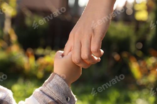 Preview: Daughter holding mother's hand outdoors, closeup view
